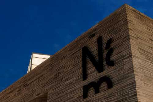 Bilde av utsnitt av bygning av Nasjonalmuseet med skilt mot blå himmel.